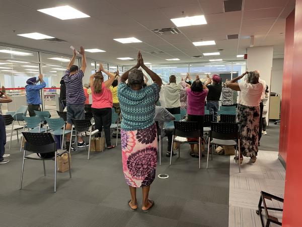 A room full of people do chair yoga.