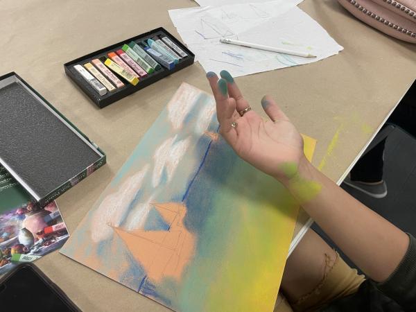 A person shows their messy fingers after rubbing a pastel portrait.